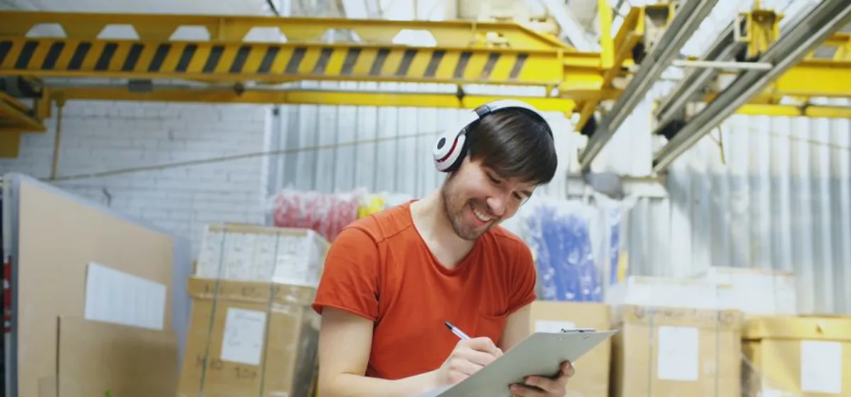 A warehouse worker smiling as he checks a clipboard of orders